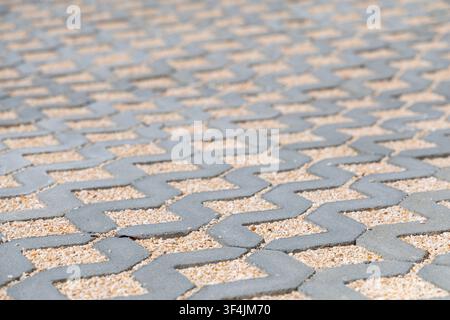 A close-up view of interlocking concrete pavers filled with small beige gravel, forming a repeating zigzag design across the ground Stock Photo