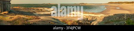 Hanko, Finland - 28.04.2019: Scenic view of rocky shores and calm sea waves meeting a sandy beach near an old wooden cabin Stock Photo