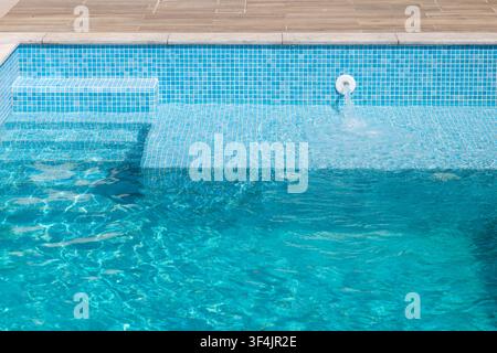 Close-up view of a modern swimming pool showing the tiled steps and a water jet creating ripples in the turquoise water Stock Photo