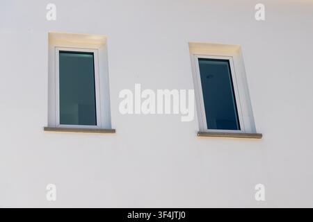 A close-up view shows two rectangular windows with dark glass set into a rough white stucco facade Stock Photo