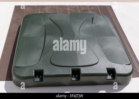 A textured, dark green plastic lid with molded wave patterns sits on a composite deck and concrete surface Stock Photo
