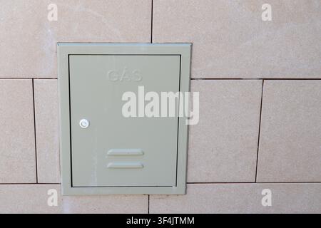 A neutral-toned tiled exterior wall features a discreetly placed, light green metal utility box labeled 'GAS' with a small lock Stock Photo
