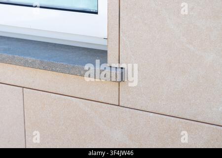 Close-up view of a contemporary building exterior showcasing textured beige stone cladding and a contrasting dark grey granite window ledge Stock Photo