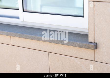 Close-up view of a contemporary building facade featuring beige stone tiles and a dark granite window ledge Stock Photo