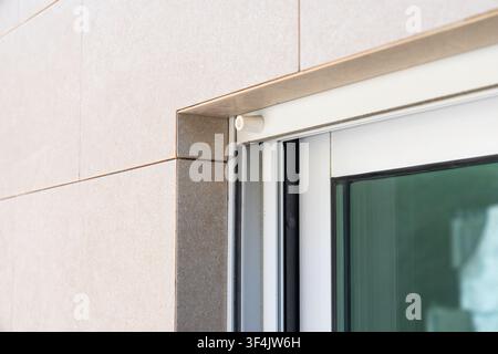 Detail of the edge of a sliding door system showing the white frame and a section of a textured beige tiled exterior wall Stock Photo