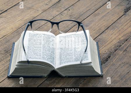 Reading eyeglasses on open English dictionary book on wooden table, symbolizing nearsightedness, education, literacy and language learning knowledge Stock Photo