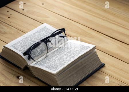 Black eyeglasses resting on open dictionary book on wooden table, concept of nearsightedness, myopia, reading, education and knowledge learning Stock Photo