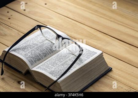 Black framed eyeglasses on open old dictionary book on rustic wooden table, symbolizing nearsighted vision, reading, education and language learning Stock Photo