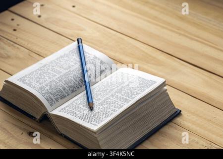 Open dictionary book with blue pencil on pages resting on rustic wooden table, showing reading, learning, education and language study concept idea Stock Photo