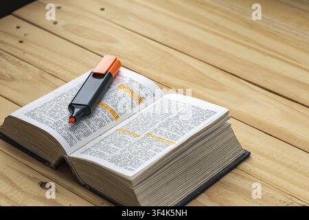 Open English dictionary with orange highlighter marker pen and highlighted words on wooden table, symbolizing language study, learning, and education. Stock Photo