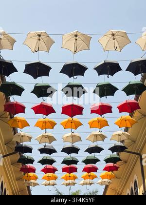 Colorful umbrellas hang from wires above a street, creating a decorative display against a clear blue sky in an urban environment Stock Photo