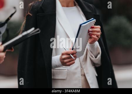 Businesswoman taking notes in a notebook during an outdoor meeting on a city street Stock Photo