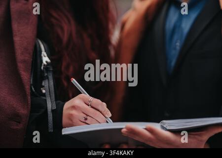 Business colleagues taking notes and signing a notebook together during an outdoor meeting Stock Photo