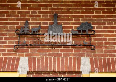 View of the metal sign for De Brandtoren featuring silhouettes of a tower, a deer, and a rabbit mounted on a red brick wall in Esbeek, Noord-Brabant, Stock Photo