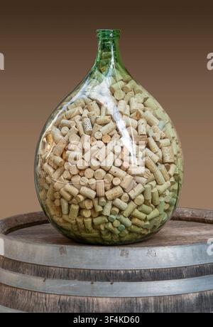 Big glass bottle filled with wine corks located on a wine barrel isolated in gradient back Stock Photo