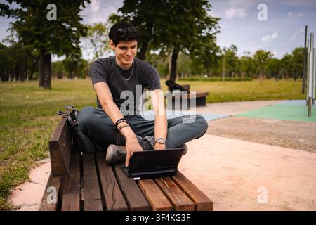 Young man using laptop smiling working remotely in park Stock Photo