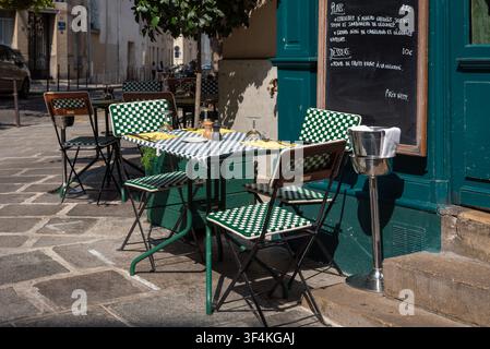 A charming outdoor restaurant terrace featuring classic green and white checkered bistro chairs and table in bright natural sunlight. Stock Photo