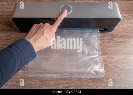 Woman pressing button on automatic vacuum sealer machine with plastic bag on wooden table Stock Photo