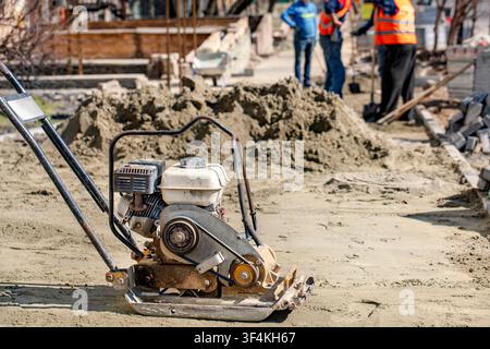 Workers operate compactor on freshly laid concrete at construction site. They prepare area for further building activities. Stock Photo