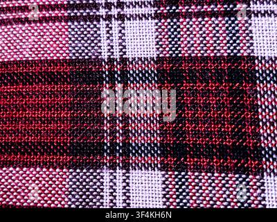Macro shot of a woven plaid fabric featuring a traditional checkered pattern in red, black, and white threads. Stock Photo