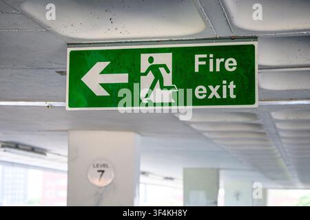 Green fire exit sign featuring a left arrow and running man symbol, car park garage Stock Photo