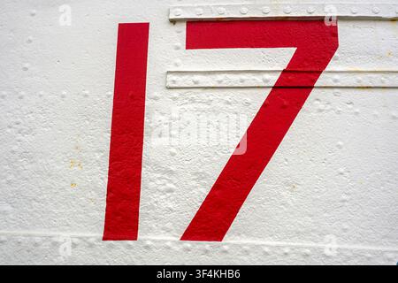 Bold red number 17 painted on a weathered white metal panel with visible rivets and texture Stock Photo