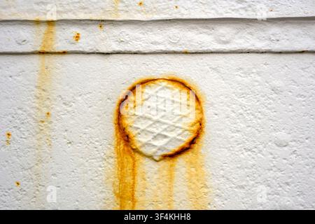 Close up of a rusty circular hatch on a white painted metal wall, showing corrosion Stock Photo