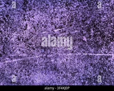 Close-up of a heavily weathered concrete or stone surface with a dark purple tint, featuring rough textures, scratches, and mottled patterns. Stock Photo