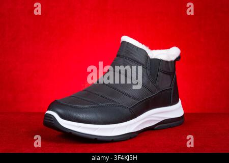 Fleece lined black winter ankle boot against red background Stock Photo