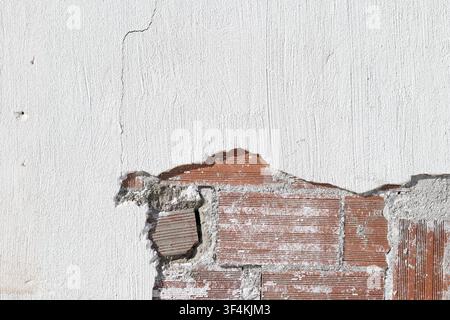 background of a damaged white plastered wall revealing red brick masonry structure Stock Photo