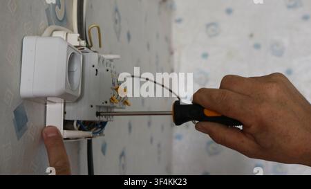 Installing a surface-mounted electrical panel on a wallpapered wall. A technician uses a screwdriver to tighten the contact on a circuit breaker. Stock Photo