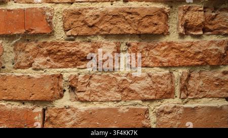 Old brickwork as a textured background. The red bricks have an uneven, chipped texture, cracks, and signs of aging. Crumbling brick wall, close-up Stock Photo