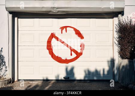 Red no entry sign spray painted on a white garage door, showing restriction, warning, and ban. Stock Photo