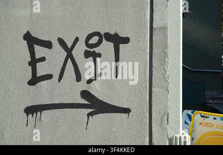 Graffiti text EXIT with an arrow pointing right, spray painted on a light grey textured urban wall in daylight Stock Photo