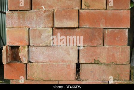 stack of red bricks without mortar. The blocks are unevenly laid, with shifts and gaps. The clay texture is uneven, with chips, scratches Stock Photo