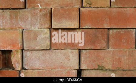 Old brickwork without mortar. Rectangular red and orange bricks are laid unevenly, with chips, cracks, and uneven gaps, creating a rough texture Stock Photo