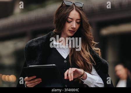 Businesswoman checking her watch while holding a tablet on a city street during workday Stock Photo