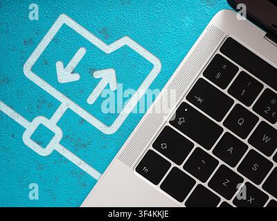 Laptop keyboard next to a folder icon with upload and download arrows. Data transfer and synchronization concept Stock Photo