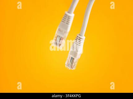 Two white Ethernet cables featuring RJ45 connectors, representing internet connection, technology, and telecommunication on yellow background Stock Photo