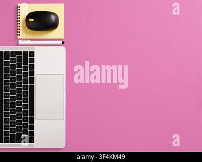 Workspace with laptop keyboard, mouse, yellow notebook, and pen arranged on a vibrant pink background with copy space Stock Photo