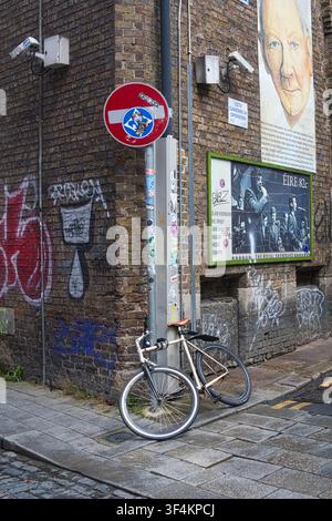 Bicycle locked against a pole on a cobblestone street corner featuring graffiti. a no entry sign and security cameras in Dublin, Ireland. Stock Photo