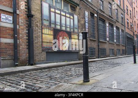 Narrow historic cobblestone street with brick buildings featuring large prints of stained glass in Dublin, Ireland. Stock Photo