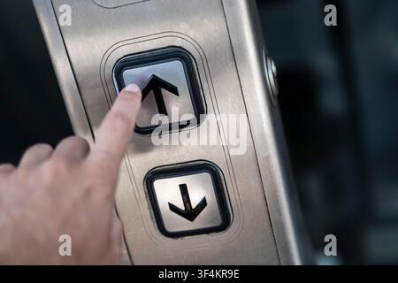 Finger pressing an up arrow button on an elevator panel illustrating modern transit infrastructure and vertical mobility. Stock Photo