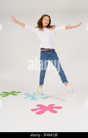 A cute girl happily jumps in stylish clothes among fun, colorful shapes on the floor. Stock Photo