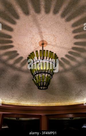 Creative chandelier made from recycled green glass bottles casting decorative shadows on an elegant ceiling interior. Stock Photo