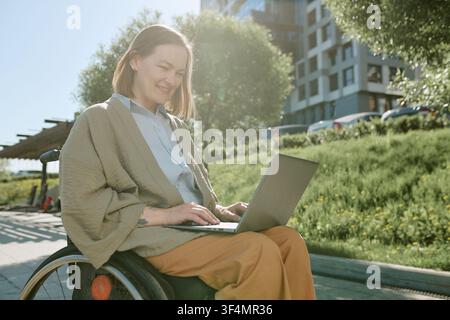 Woman with Disability Using Laptop Outdoors for Remote Work Stock Photo