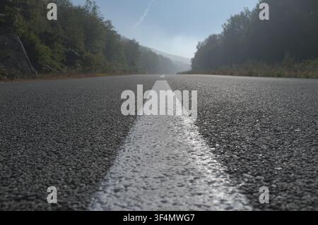 bottom view of an asphalt road surface with a white center line on a misty morning, Bosnia and Herzegovina Stock Photo