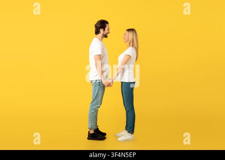 Happy Couple Holding Hands And Smiling At Each Other, Yellow Background, Love Concept Stock Photo
