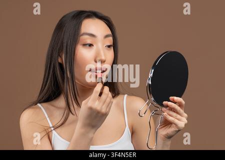 Young Asian Woman Applying Lipstick In Front Of Mirror At Home, Beauty Concept Stock Photo