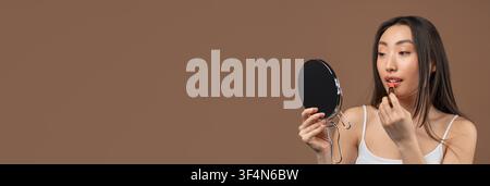 Young Asian Woman Applying Lipstick In Front Of Mirror At Home, Beauty Concept Stock Photo